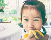 Adorable asian girl eating a ripe banana. vintage tone.