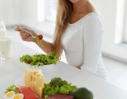 Healthy Woman Eating Salad In Kitchen, Food Products On Table