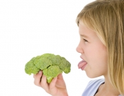 Young girl holding broccoli and sticking tongue out