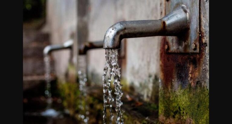 Torneira enferrujada com água escorrendo, simbolizando a contaminação por PFAS na água potável